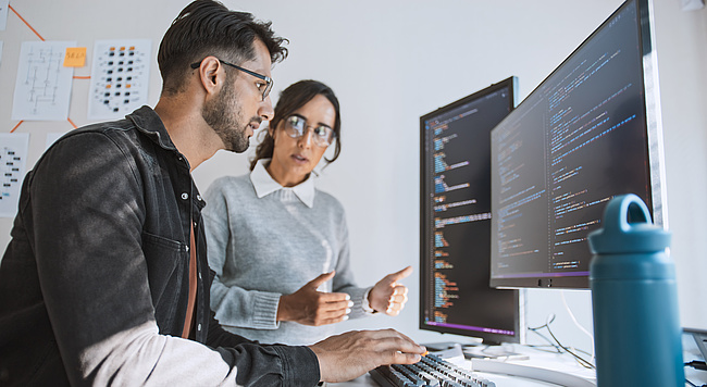 Zwei Mitarbeitende diskutieren den Programmcode einer KI-Lösung Zwei Mitarbeitende diskutieren den Programmcode einer KI-Lösung